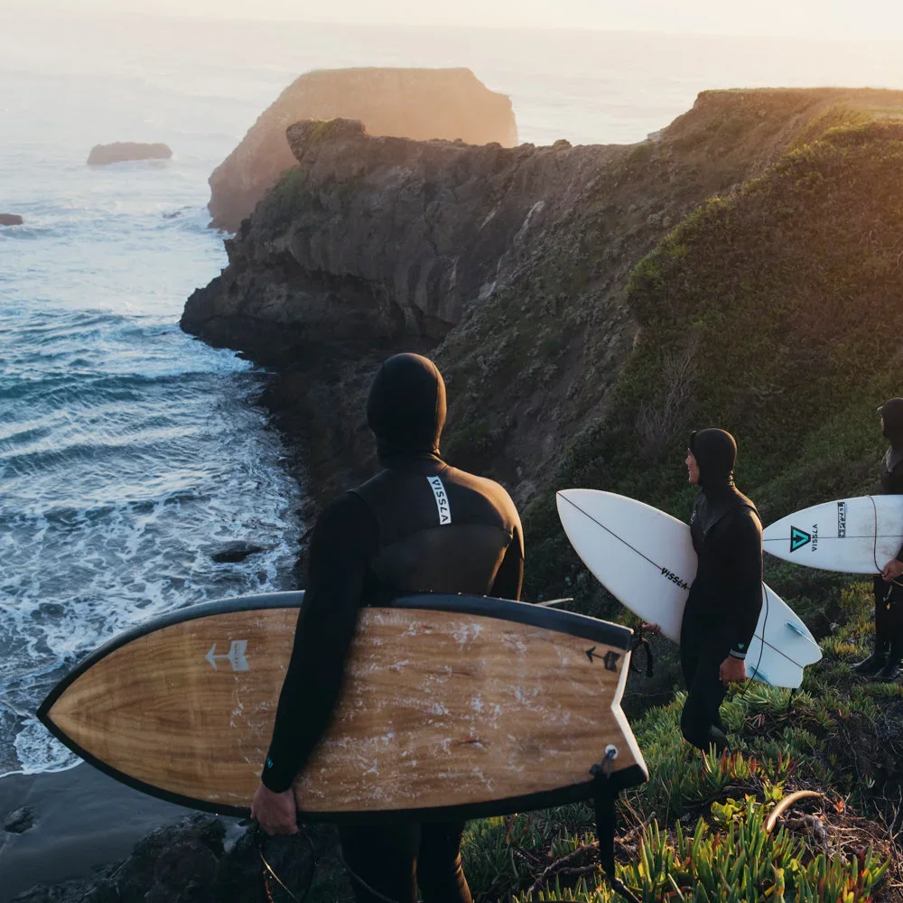 Surfistas en el acantilado con tablas de surf y trajes de neopreno con capucha de Vissla